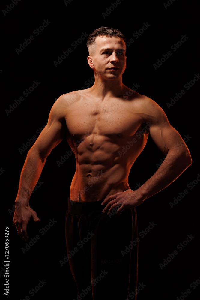 Fototapeta premium Adult male athlete bodybuilder posing on a orange light