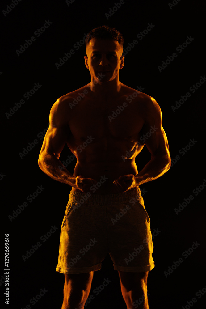 Fototapeta premium Adult male athlete bodybuilder posing on a orange light 