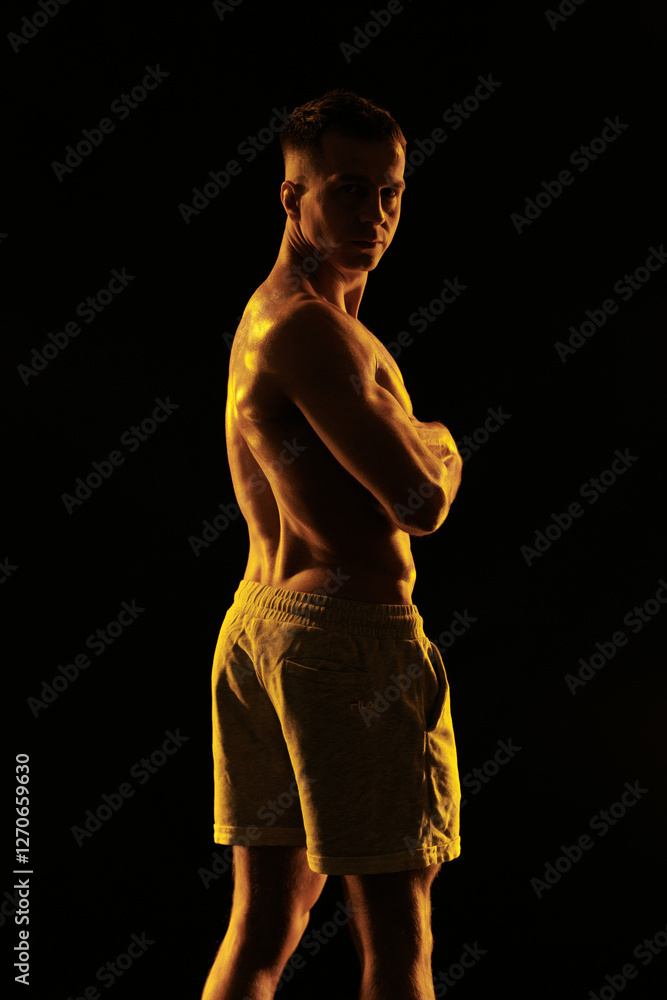 Naklejka premium Adult male athlete bodybuilder posing on a orange light 