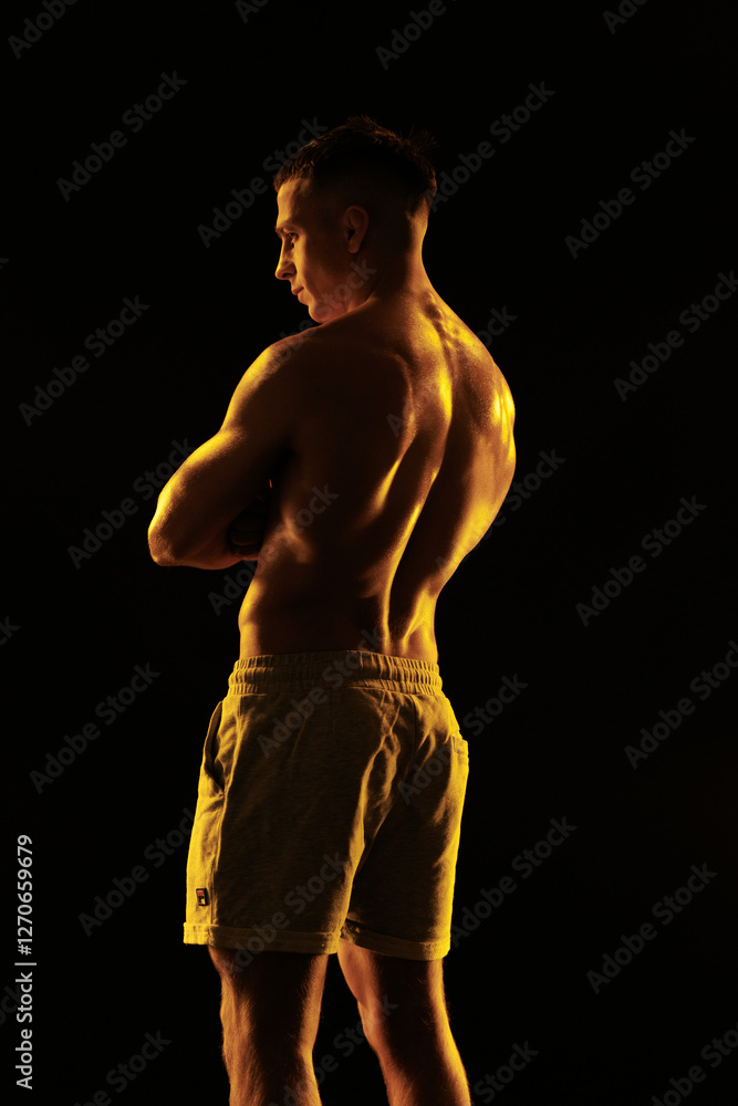 Fototapeta premium Adult male athlete bodybuilder posing on a orange light 