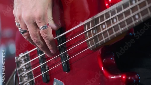 Vivid image capturing musician playing bass guitar with detailed focus on strings. Vibrant red surface of the instrument highlights the artistic elements of passionate live music performance.