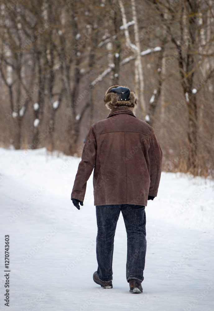 A man wearing a brown coat and hat walks on a snowy path A man wearing a brown coat and hat walks on a snowy path