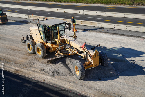 Bild auf Leinwand Capturing a motor grader spreading gravel to create a smooth and level surface foundation for a new asphalt layer on a construction site