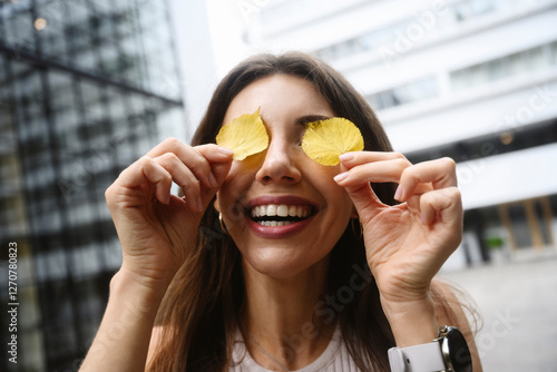 Smiling woman hiding her eyes with yellow autumn leaves outdoors photo