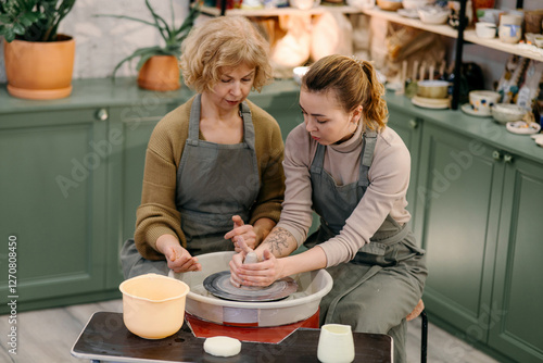 Wallpaper Mural Mentor guiding elderly student in sculpting pottery on electric spinning wheel Two generations of women participate in hands-on ceramics training, shaping clay on a wheel Torontodigital.ca