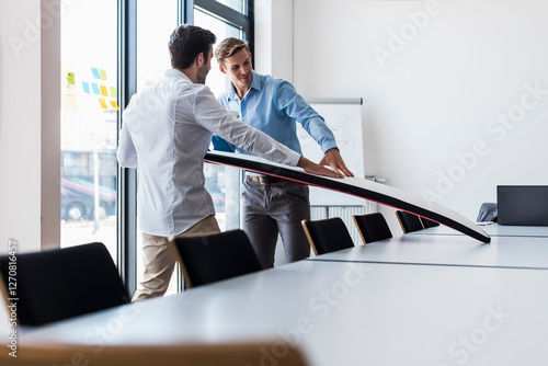 Smiling businessmen examining surfboard in office photo