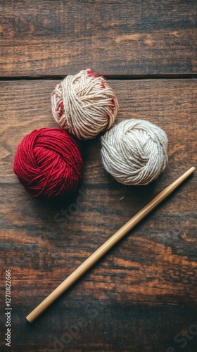 Yarn balls and knitting needles arranged on a rustic wooden surface for creat...