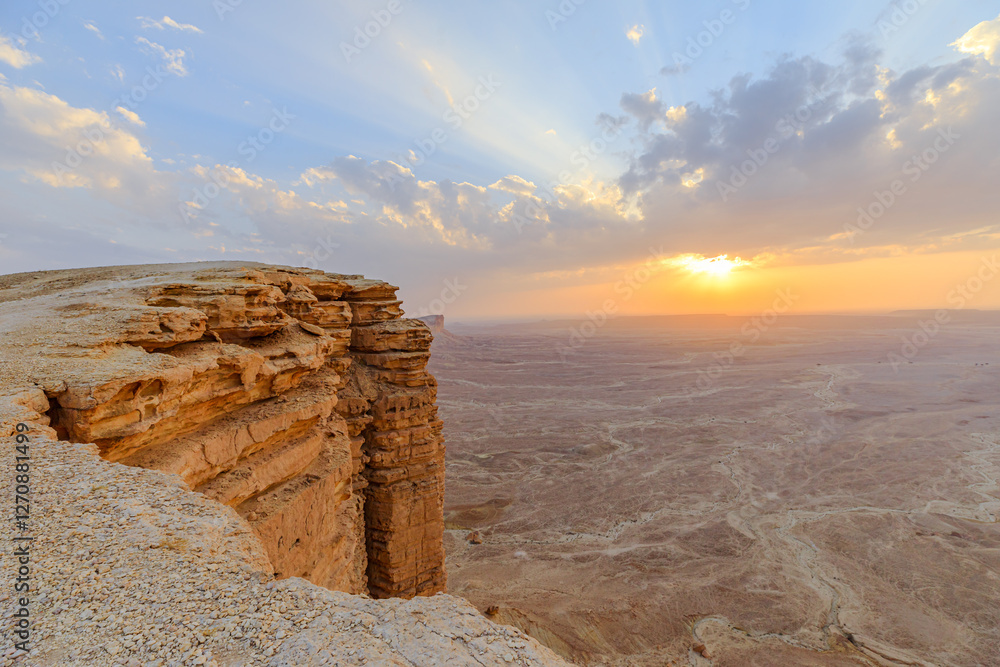 Golden hour sunlight illuminates the Tuwaiq escarpment at sunset, casting long shadows across the desert landscape near Riyadh, Saudi Arabia, a breathtaking view from the edge of the world