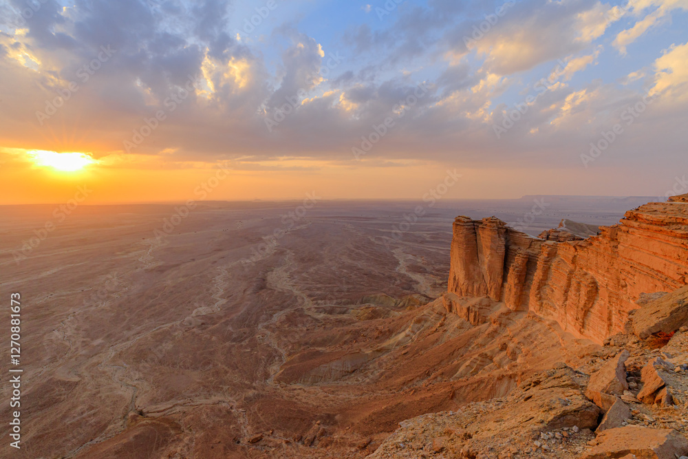 Golden sunset illuminating a vast desert landscape from the edge of the world escarpment, highlighting the dramatic cliffs of the Tuwaiq mountain range near Riyadh, Saudi Arabia