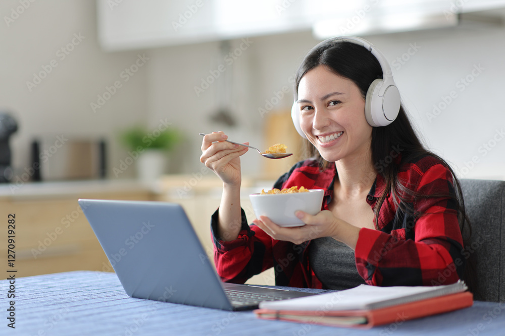 Happy asian student eating cereals looking at you Happy asian student eating cereals looking at you