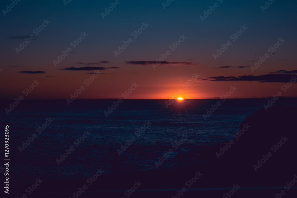 Fototapeta premium A red ball of fire plunging tin the water of El Cotillo beach, Fuerteventura, Canary Islands. Orange and pink sky, amazing scenic view.