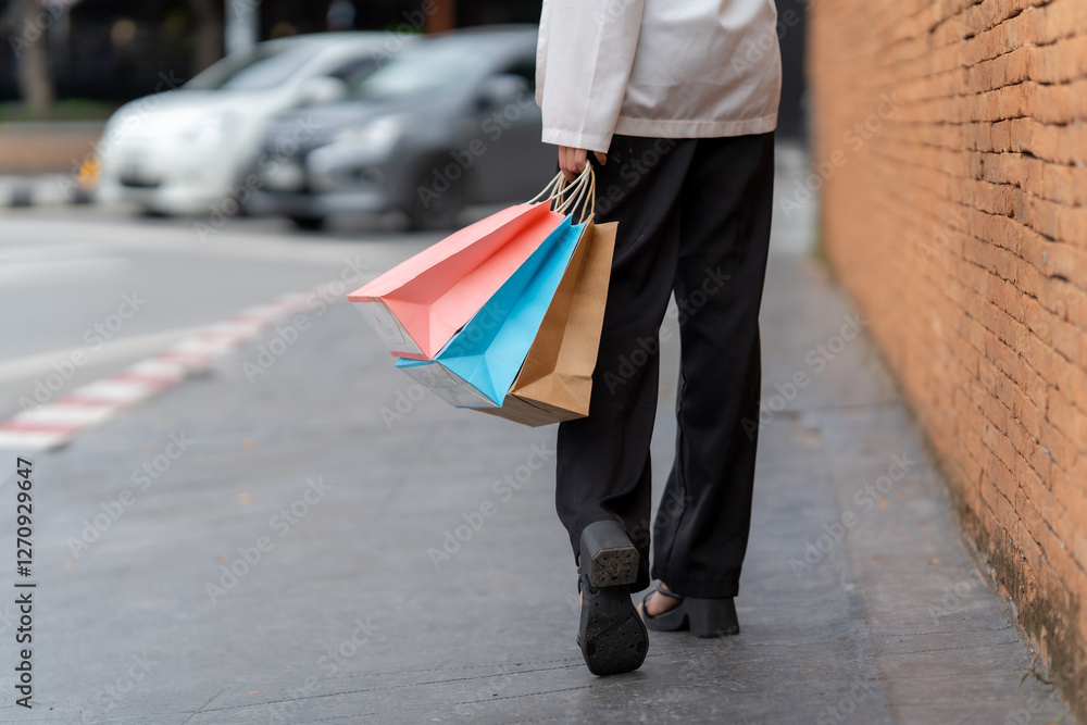 Retail Therapy Stroll: A person embarks on a shopping adventure, clutching vibrant bags while navigating an urban sidewalk against a backdrop of brick and parked vehicles.