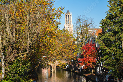Vibrant autumn trees in red yellow and orange frame a canal bridge with the Dom Tower rising above in Utrecht Netherlands