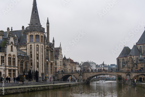 Medieval gothic buildings and a stone arch bridge line the historic canal on a gray winter day in Ghent Belgium