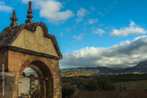 An ancient stone arch gateway frames a sweeping view of the green valleys and mountains around Ronda in Andalusia Spain