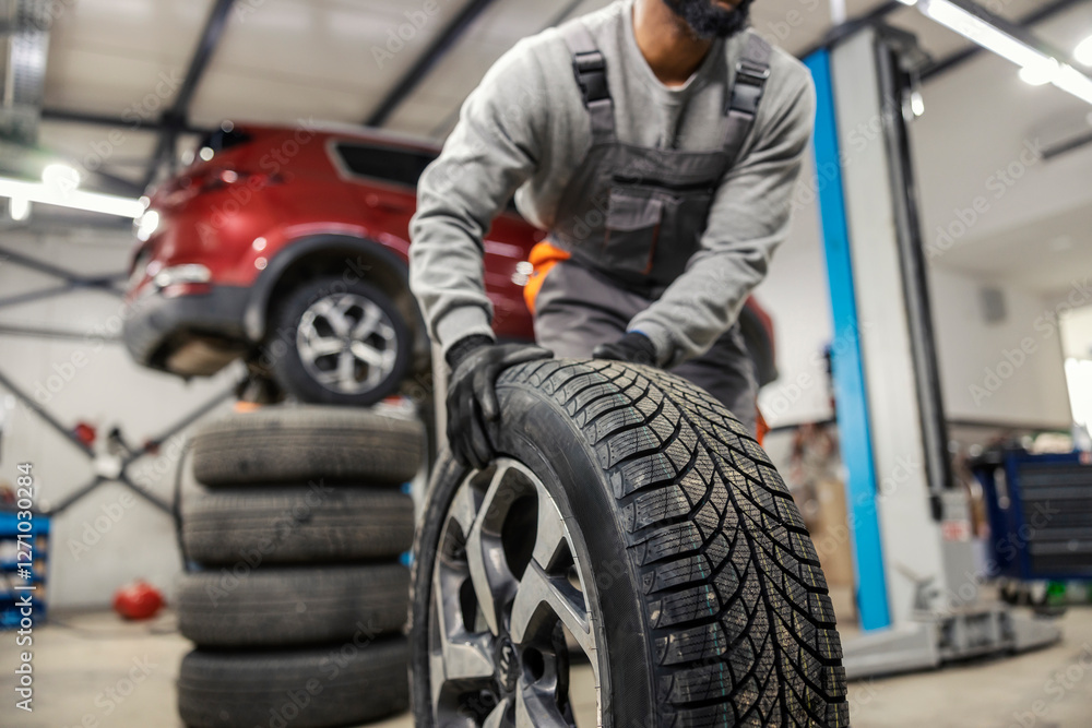 Cropped picture of unknown auto mechanic rolling tire at mechanic workshop. Cropped picture of unknown auto mechanic rolling tire at mechanic workshop.