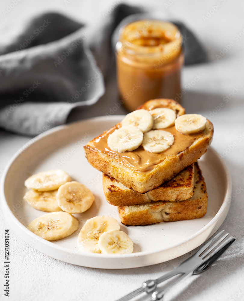 Peanut butter toast with banana on a plate on a light background with jar and napkin close up. Peanut butter toast with banana on a plate on a light background with jar and napkin close up.