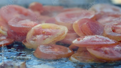 Delicious red ripe tomato slices fry on large hot griddle outdoors