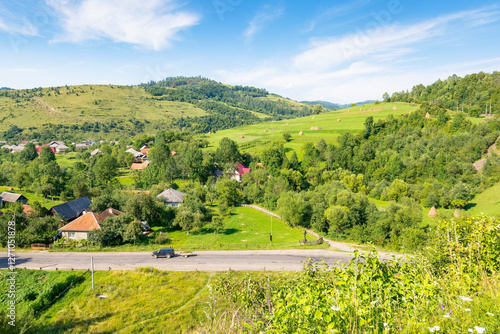 mountainous countryside landscape of ukraine in summer. sunny day. scenery with grassy rural field and forest on the hill. village in the valley. clouds on blue afternoon sky. alpine climate