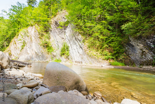 Obraz na płótnie mountain river with stones on the shore. outdoor adventure. scenic landscape with forest on the rocky mountain slope. nature scenery on a sunny summer day. vacation season w salonie