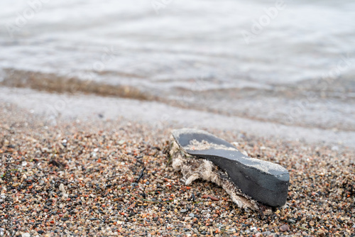 Billede på lærred Worn shoe sole discarded by sea lies on beach, with ocean waves in background, i