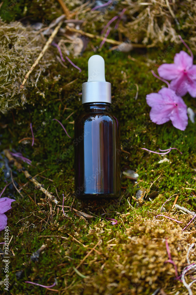 Natural skincare serum resting on moss with delicate pink flowers around Natural skincare serum resting on moss with delicate pink flowers around