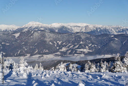 Sunny snowy winter mountain landscape, long distance view,  icy cold, strong wind and clear blue sky by Stuhleck, Styria, Austria. In the background the peak of the mountain Rax is visible.