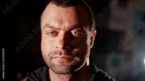 Male portrait with dramatic lighting. Half of the face is illuminated, emphasizing the harsh look and skin texture. A dark background enhances the effect of depth and contrast.