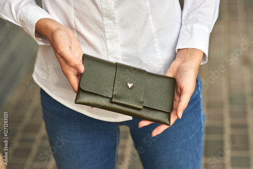 Woman holding elegant green leather wallet, wearing white shirt and blue jeans, outdoor street scene concept