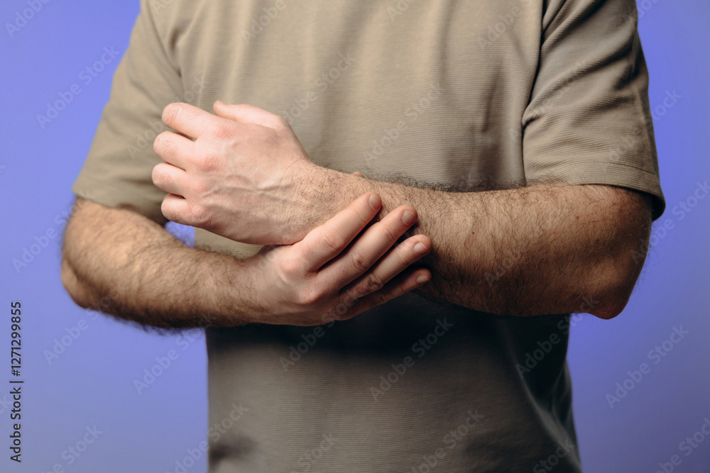 Fototapeta premium A man holds his wrist in pain. The hand tightly clasps the affected area, emphasizing the soreness and need for support. Pain and suffering in the wrist interfere with professional activities.