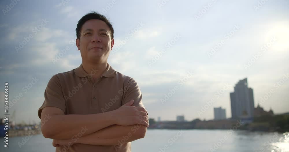 Man poses confidently by riverbank in urban setting during late afternoon light Man poses confidently by riverbank in urban setting during late afternoon light