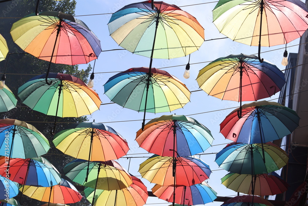 Obraz premium A vibrant display of rainbow-colored umbrellas hanging above a bustling street