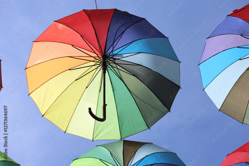 A vibrant display of rainbow-colored umbrellas hanging above a bustling street A vibrant display of rainbow-colored umbrellas hanging above a bustling street