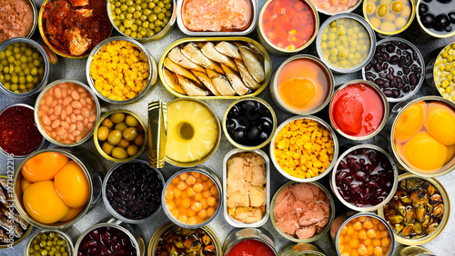 A large set of pickled and canned foods on the background. Metal cans with canned vegetables, beans, fish, seafood and fruit. Top view. © Yaruniv-Studio