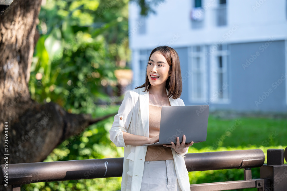 A woman is holding a laptop while standing on a fence A woman is holding a laptop while standing on a fence