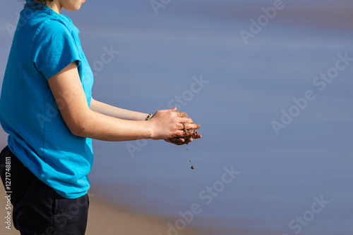 A child's hands hold moist soil, a few clumps falling towards the ground, the sea provides a blue background on a bright day. photo