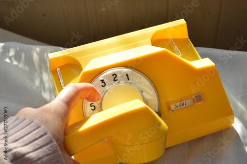 A person dials a number on a vibrant yellow vintage rotary phone, capturing the essence of a bygone era. photo