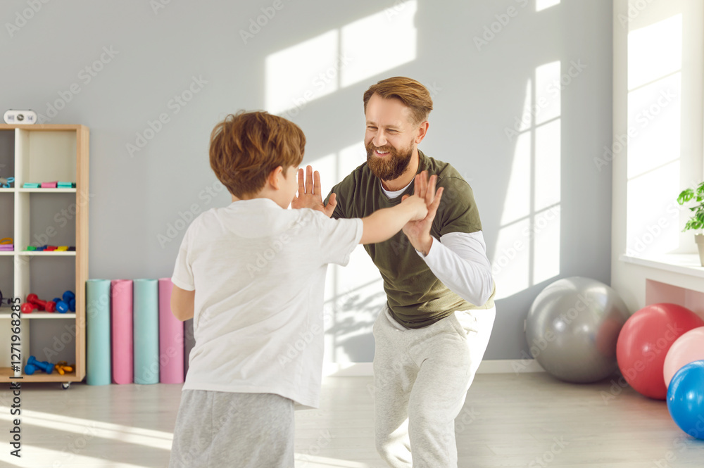 Obraz premium Happy smiling young man with child boy wearing sportswear doing boxing sport exercise in gym during workout. Father and son exercising together. Family health and body care concept.