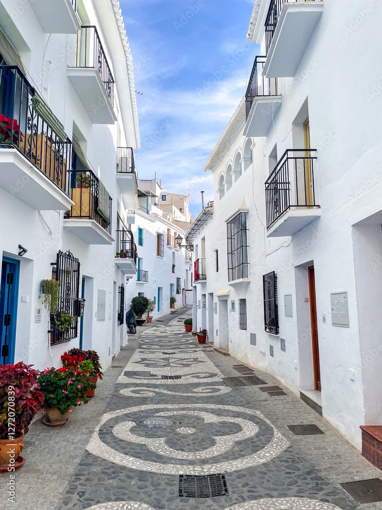 Fototapeta premium Charming cobblestone street with white houses and colorful flowers in the picturesque village of Frigiliana, Andalusia, Spain on a sunny day with blue sky