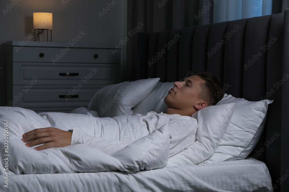 Fototapeta premium Young man sleeping in soft bed at night