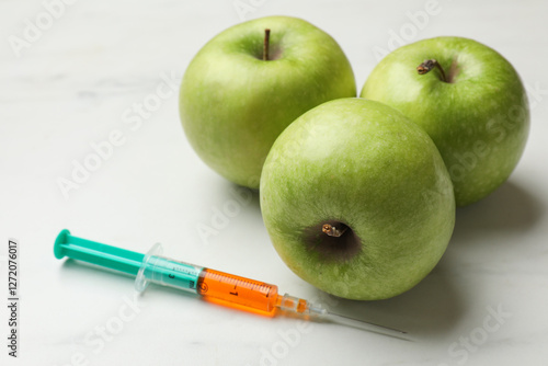 GMO concept. Green apples and syringe on white marble table, closeup