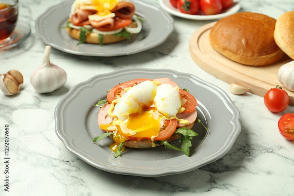 Tasty brunch. Poached egg, ham, tomato, arugula and bun on white marble table, closeup Tasty brunch. Poached egg, ham, tomato, arugula and bun on white marble table, closeup