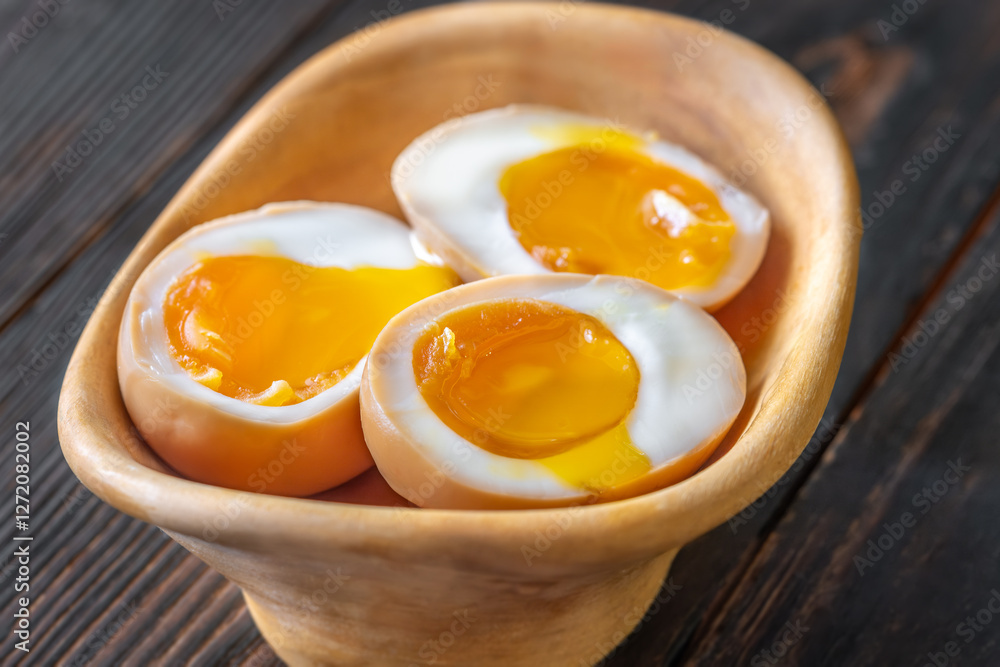 Halved ajitsuke tamago ramen eggs with golden yolks in wooden bowl Halved ajitsuke tamago ramen eggs with golden yolks in wooden bowl