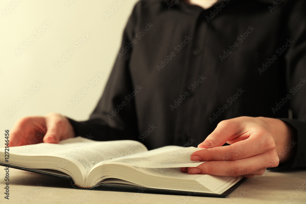 Woman reading Holy Bible in English language at beige table, closeup Woman reading Holy Bible in English language at beige table, closeup