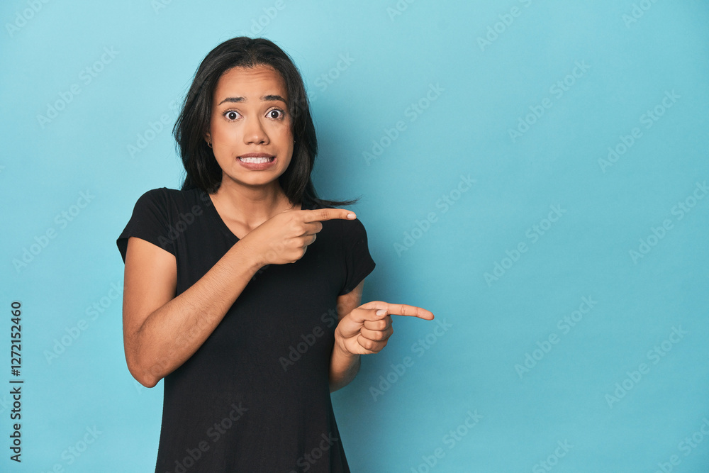 Filipina young woman on blue studio shocked pointing with index fingers to a copy space. Filipina young woman on blue studio shocked pointing with index fingers to a copy space.