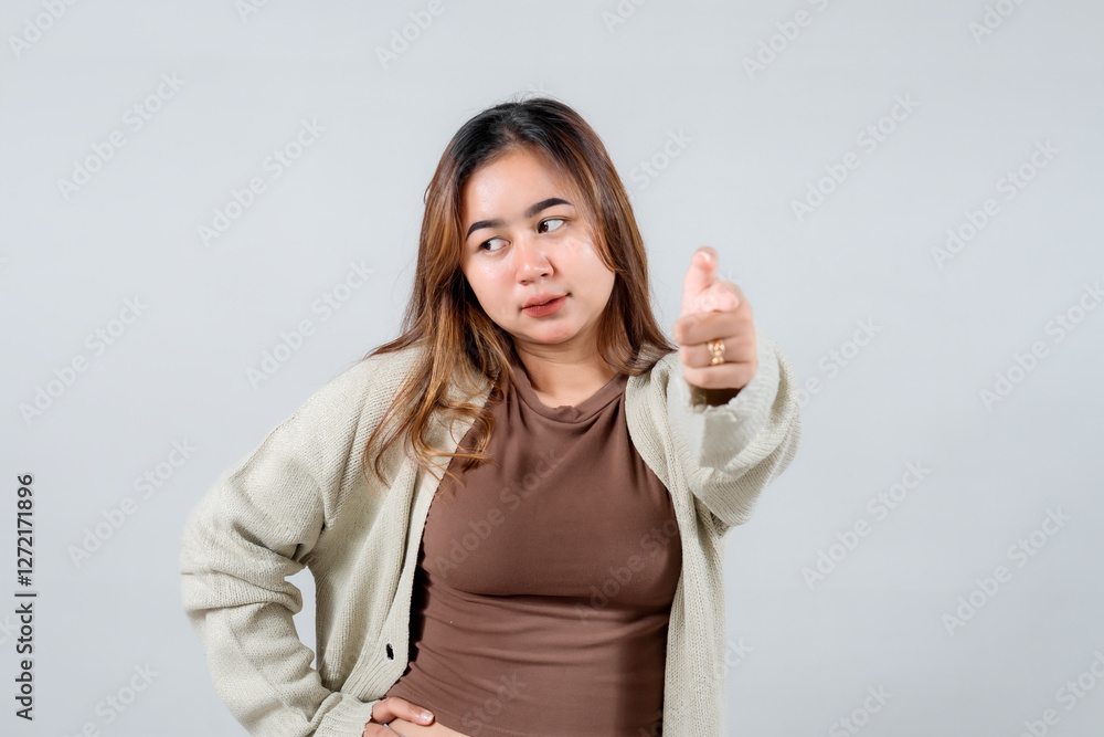 A young woman points directly at the camera with a confident and engaging expression, wearing a cozy sweater. She connects with the viewer against a neutral background A young woman points directly at the camera with a confident and engaging expression, wearing a cozy sweater. She connects with the viewer against a neutral background