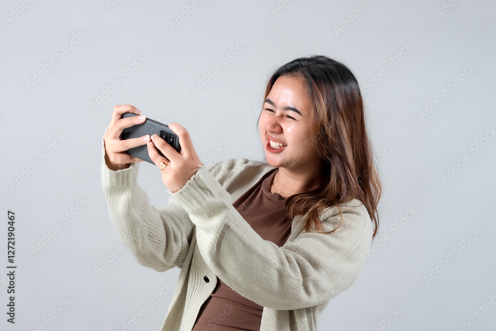 A young woman expresses intense concentration and determination while looking at her smartphone, showcasing a strong emotional reaction against a neutral background A young woman expresses intense concentration and determination while looking at her smartphone, showcasing a strong emotional reaction against a neutral background