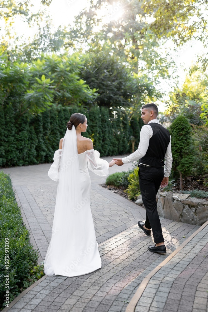 Groom tenderly embracing bride while holding hands in park during wedding ceremony Groom tenderly embracing bride while holding hands in park during wedding ceremony
