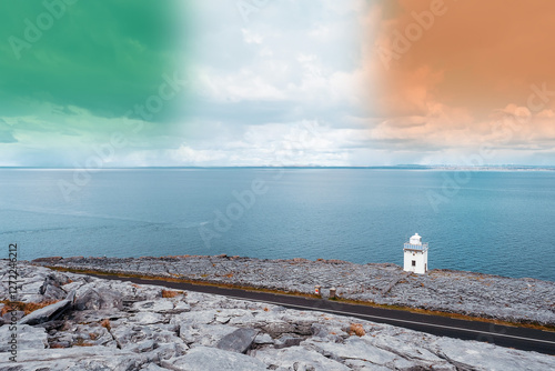 Black head lighthouse between small road and Atlantic ocean. Wild Atlantic Way route, Ireland. Blue cloudy sky with Irish flag colors. Nobody. Famous rough stone terrain. Irish nature photo