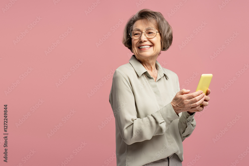 Happy senior woman using smartphone looking away smiling on pink background Happy senior woman using smartphone looking away smiling on pink background